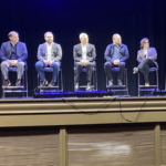 A group of professional organization leaders appear seated on a stage, facing a crowd who sit out of frame.