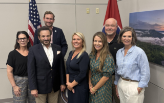 A group of professionally-dressed men and women smile for the camera. They are standing between the US flag and the Tennessee state flag.